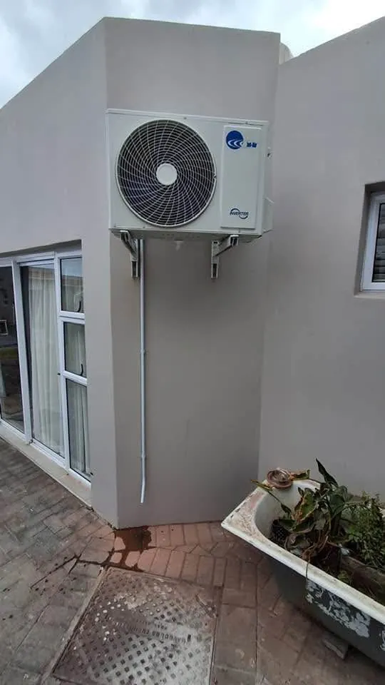 Inverter aircon outdoor unit on wall brackets beside a sliding door with tidy white pipe cover