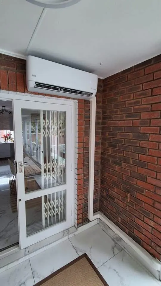 Aircon indoor unit mounted above a door on a red brick wall