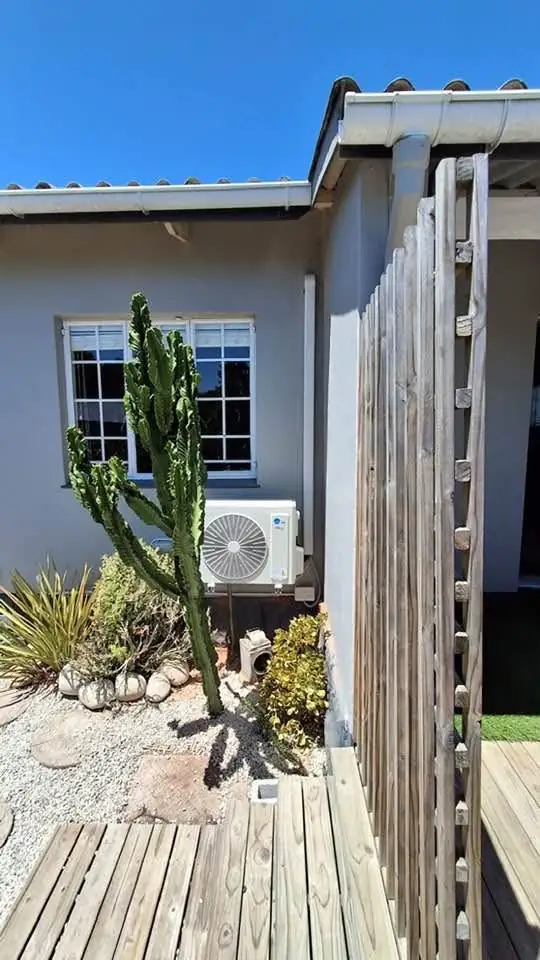 Aircon outdoor unit installed in a garden bed beside a cactus